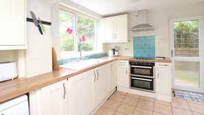 A modern kitchen with white cabinets, a wooden countertop, a built-in oven, and a window with a view of greenery.