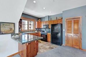 A kitchen with wooden cabinets, a black refrigerator, and a granite countertop. - 3 Bedroom Condo on Main Street in Breckenridge - Pool, Hot Tubs, Fitness Center & More! (Breckenridge)