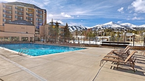 A pool area with lounge chairs and a view of snow-capped mountains. - 3 Bedroom Condo on Main Street in Breckenridge - Pool, Hot Tubs, Fitness Center & More! (Breckenridge)
