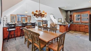 A spacious dining area with a large wooden table and chairs, a chandelier, and a kitchen with wooden cabinets and a window. - 3 Bedroom Condo on Main Street in Breckenridge - Pool, Hot Tubs, Fitness Center & More! (Breckenridge)