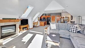 A spacious living area with a fireplace, a large gray sofa, and a dining area in the background. - 3 Bedroom Condo on Main Street in Breckenridge - Pool, Hot Tubs, Fitness Center & More! (Breckenridge)