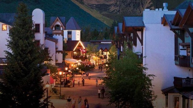 A town square with buildings, a central illuminated area, and mountains in the background.