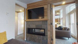 A modern living room with a stone fireplace, a flat-screen TV mounted above it, and a sofa with cushions.