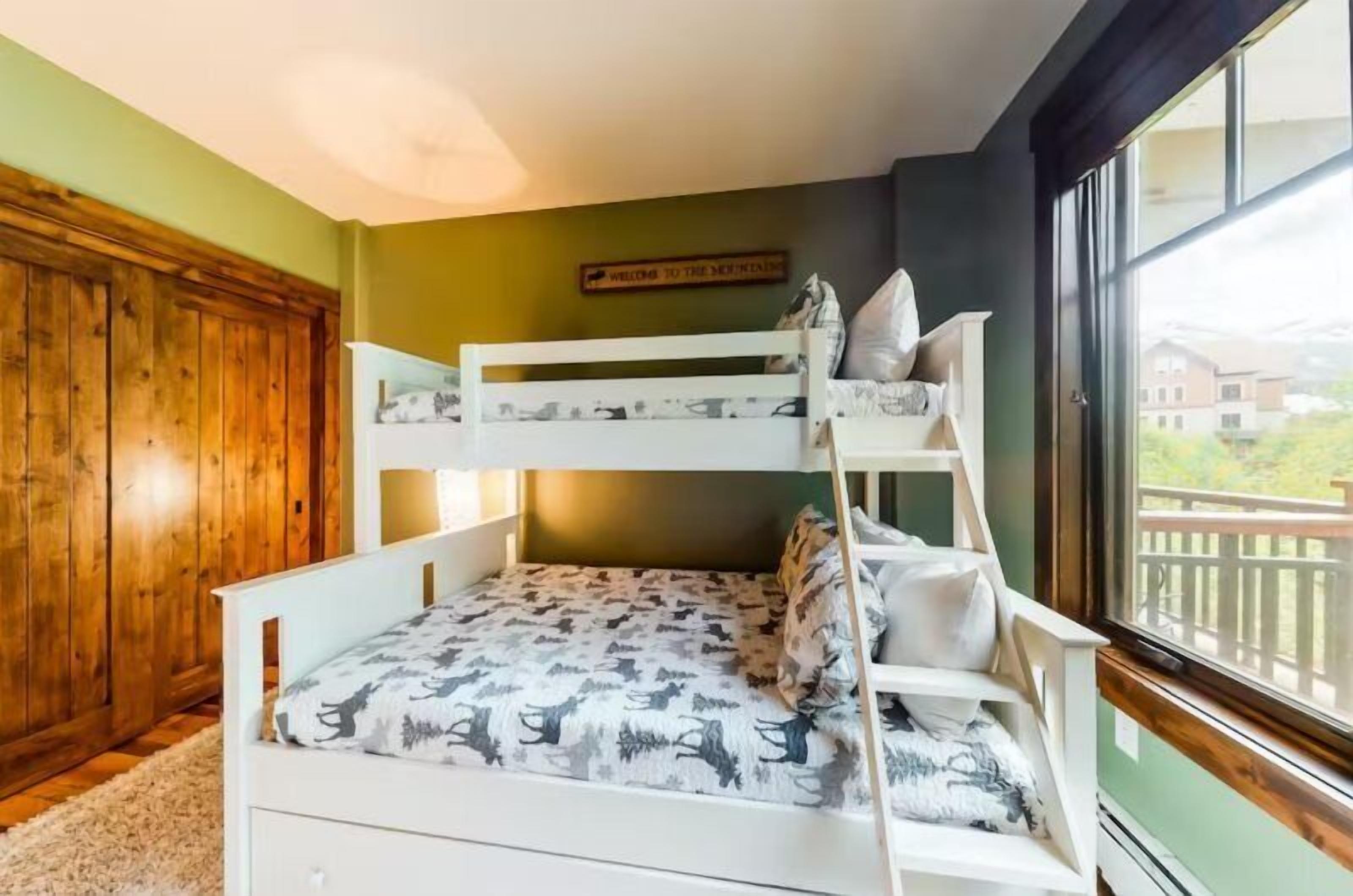 Quarto com beliche, parede verde, guarda-roupa de madeira e janela com vista.