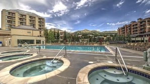 A hotel with multiple swimming pools, a large central pool, and a mountainous backdrop. - 2 Bedroom Luxury Condo on Main Street at Maggie Pond - Walk to Lift! (Breckenridge)