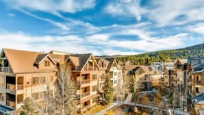 A row of wooden cabins with balconies, set against a backdrop of a clear sky and a forested mountain range. - 2 Bedroom Luxury Condo on Main Street at Maggie Pond - Walk to Lift! (Breckenridge)