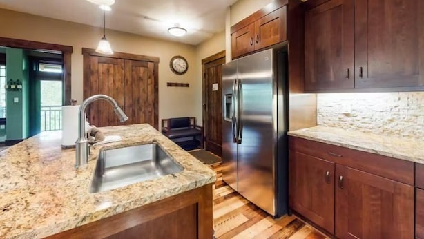 A kitchen with granite countertops, stainless steel appliances, wooden cabinets, and a built-in island with a sink. - 2 Bedroom Luxury Condo on Main Street at Maggie Pond - Walk to Lift! (Breckenridge)
