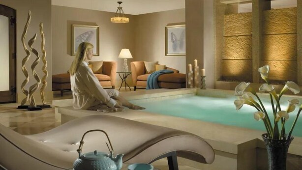 A serene spa area with a massage chair, a small table with a teapot and cup, a lounge chair, a sofa, and a decorative vase with flowers. - Arrabelle at Vail Luxe 3 Bedroom Residence With Ski-in, Ski-out Access (Vail)