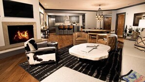 A modern living room with a fireplace, leather sofas, a round coffee table, and a kitchen area in the background. - Arrabelle at Vail Luxe 3 Bedroom Residence With Ski-in, Ski-out Access (Vail)
