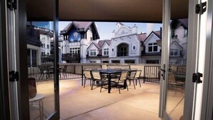 A covered patio with a round table and chairs, a view of European-style buildings, and a glass door entrance. - Arrabelle at Vail Luxe 3 Bedroom Residence With Ski-in, Ski-out Access (Vail)