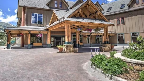 A large building with a covered entrance, multiple windows, and a stone chimney. - Water House Luxury 2 Bedroom on Main Street - Walk to Quicksilver Lift! (Breckenridge)