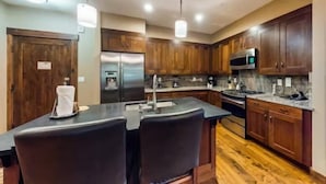 A modern kitchen with wooden cabinets, stainless steel appliances, and a central island with bar stools. - Water House Luxury 2 Bedroom on Main Street - Walk to Quicksilver Lift! (Breckenridge)