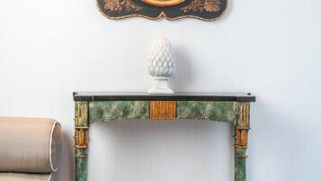 A room with a green and gold ornate table, a white vase, and a mirror with a gold frame.