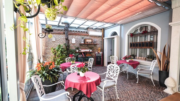 Un patio coperto con pavimento in mattoni, sedie in metallo bianco e tavoli con tovaglie rosse.