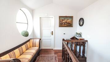 Un pasillo con un banco de madera, un ventanal circular, una puerta y una pequeña mesa con un jarrón.