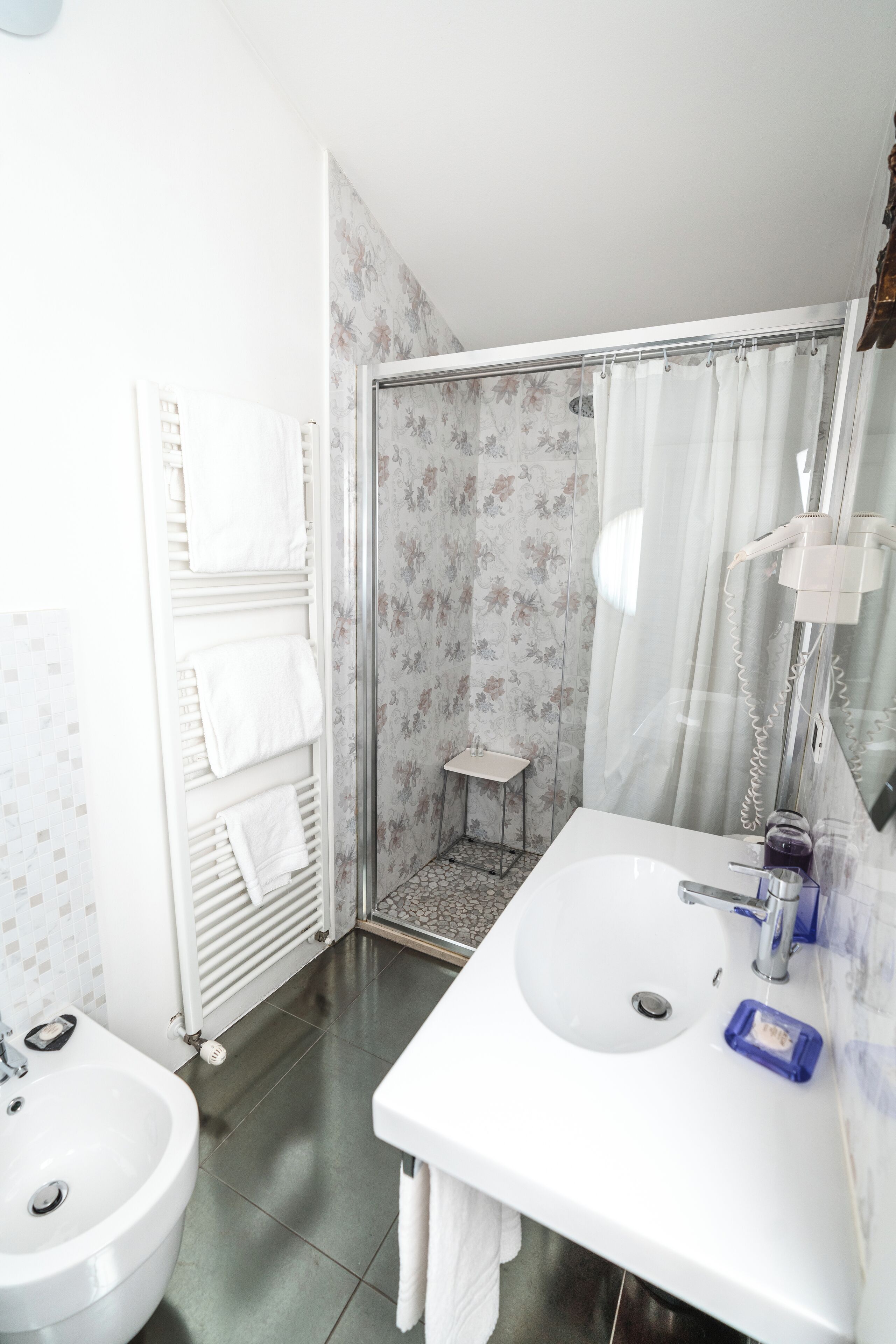 A bathroom with a shower, two sinks, a bidet, and a towel rack.