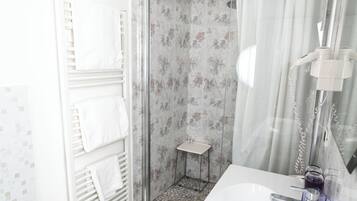A bathroom with a shower, two sinks, a bidet, and a towel rack.