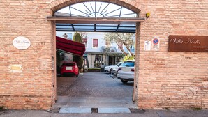 Ingresso di un edificio in mattoni con la segnaletica Villa Noesis, una zona relax esterna coperta e auto parcheggiate.