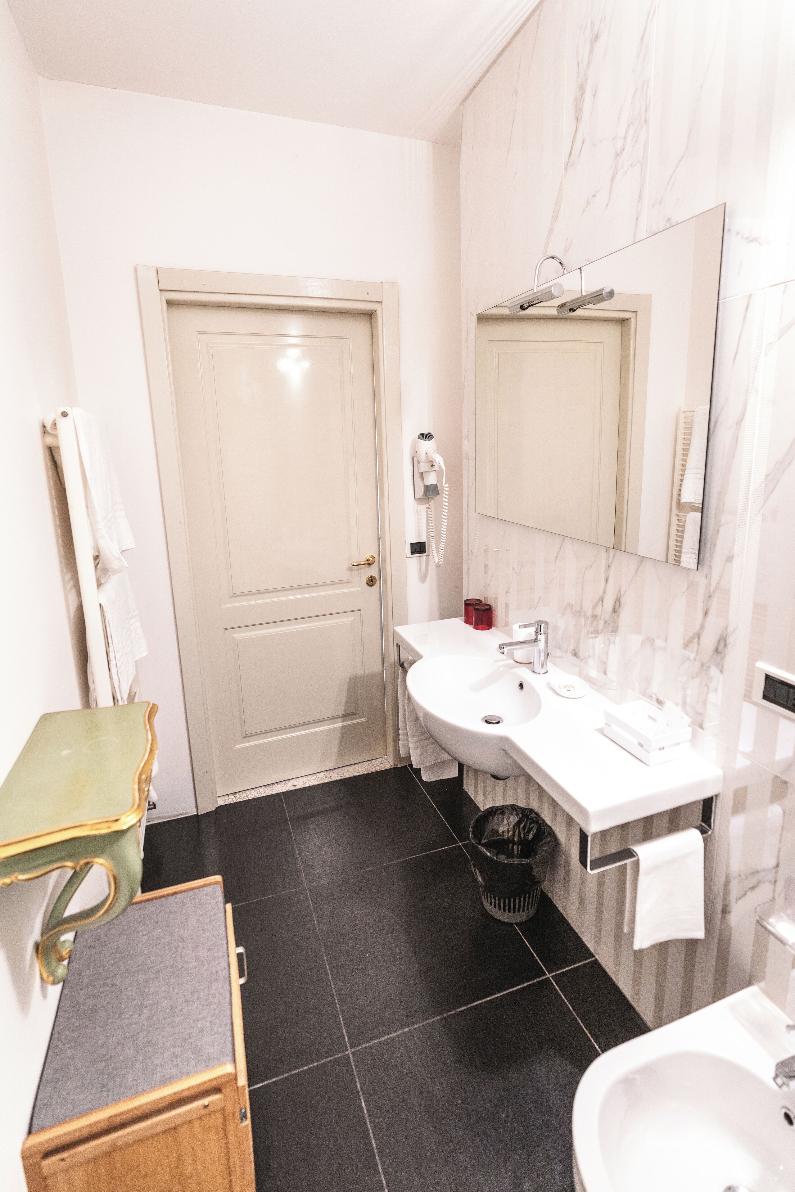 A bathroom with a white door, a sink, a mirror, and a trash bin.