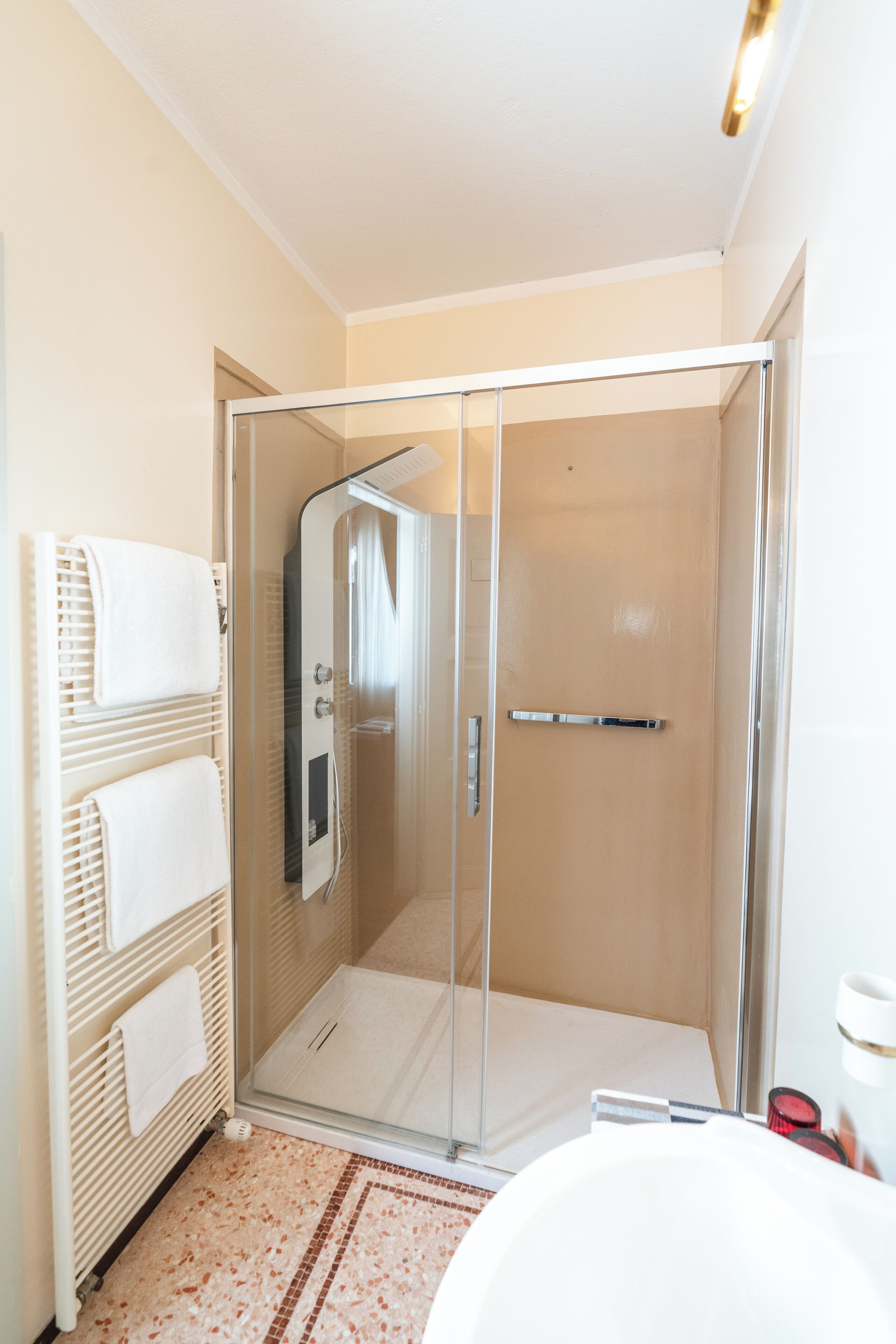 Un bagno moderno con cabina doccia in vetro, una vasca da bagno bianca e un portasciugamani con asciugni piegati.
