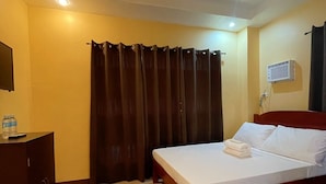 Une chambre d’hôtel avec un lit, une commode en bois, une bouteille d’eau et un climatiseur fixé au mur.