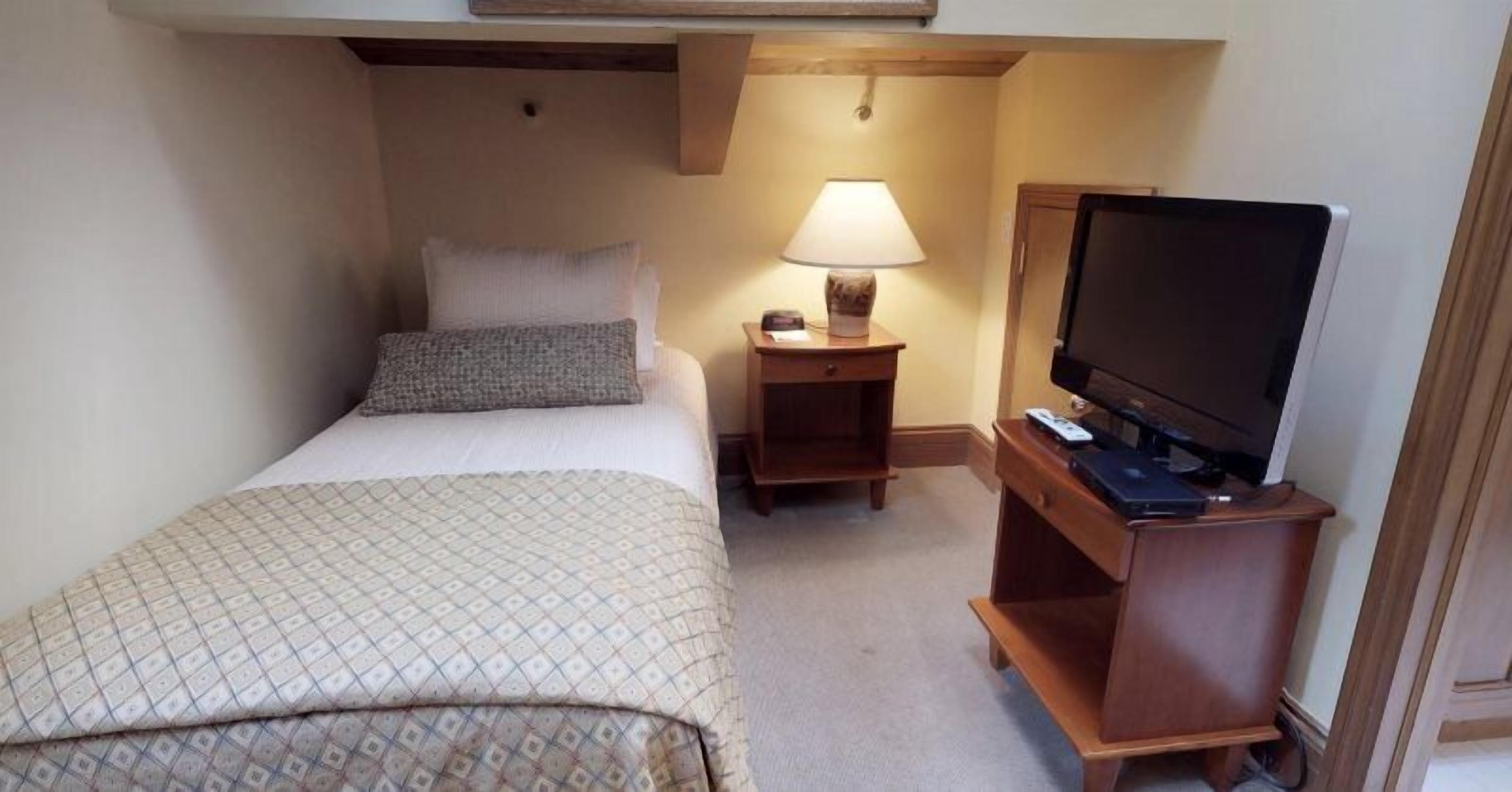 A hotel room with a bed, a bedside lamp, a TV on a wooden stand, and a small table.