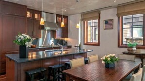 Una cocina moderna con armarios de madera oscura, una isla central con taburetes, iluminación colgante y un área de comedor con mesa y sillas de madera.