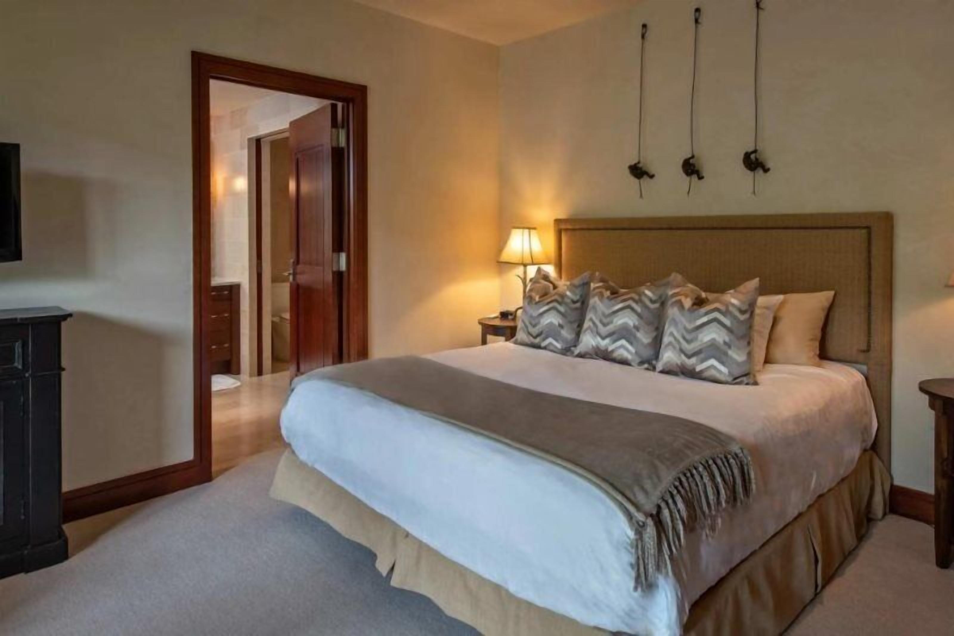A hotel room with a large bed, a nightstand with a lamp, a wardrobe, and a television on the wall.