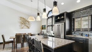 A modern kitchen with a central island, stainless steel appliances, pendant lighting, and a dining area with chairs. - 5 Bedroom Ski-in/ski-out Luxury Townhome in The Meadows Townhomes (Avon)