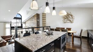 A modern kitchen with granite countertops, a dining area with a table and chairs, and pendant lighting. - 5 Bedroom Ski-in/ski-out Luxury Townhome in The Meadows Townhomes (Avon)