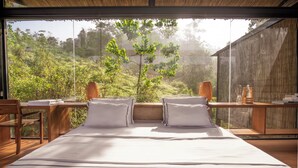 Een slaapkamer met een groot bed, houten meubels en uitzicht op een weelderige tuin.