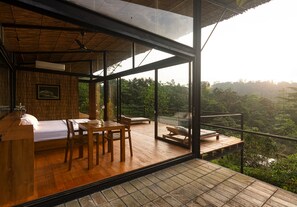 Une chambre moderne avec un plancher en bois, un lit, un bureau et une grande fenêtre donnant sur un paysage boisé.