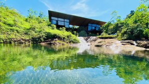 Een modern gebouw met een glazen gevel, gelegen aan een heldere rivier met omliggend groen.