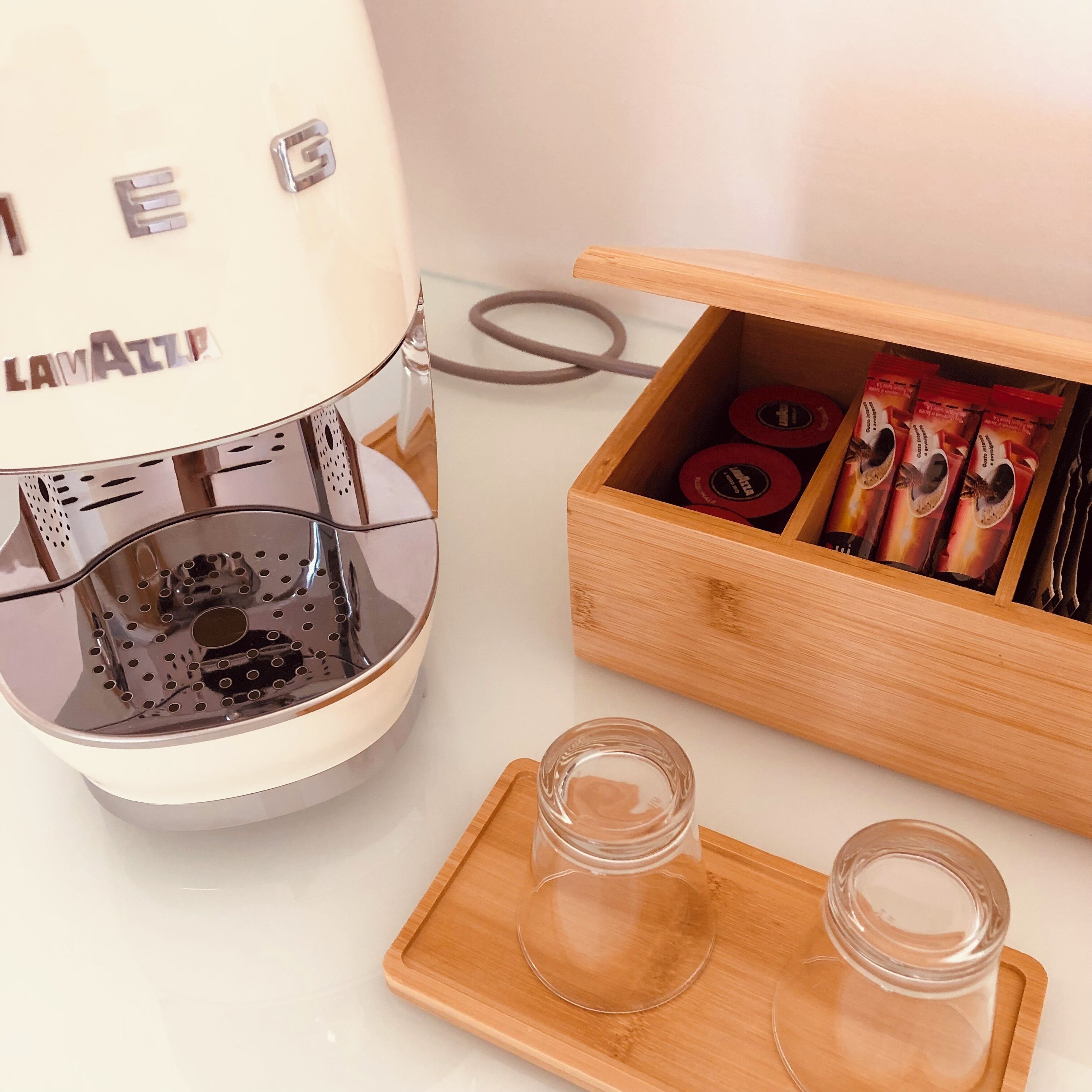 A white coffee machine with a tray and two empty glasses on a wooden tray.