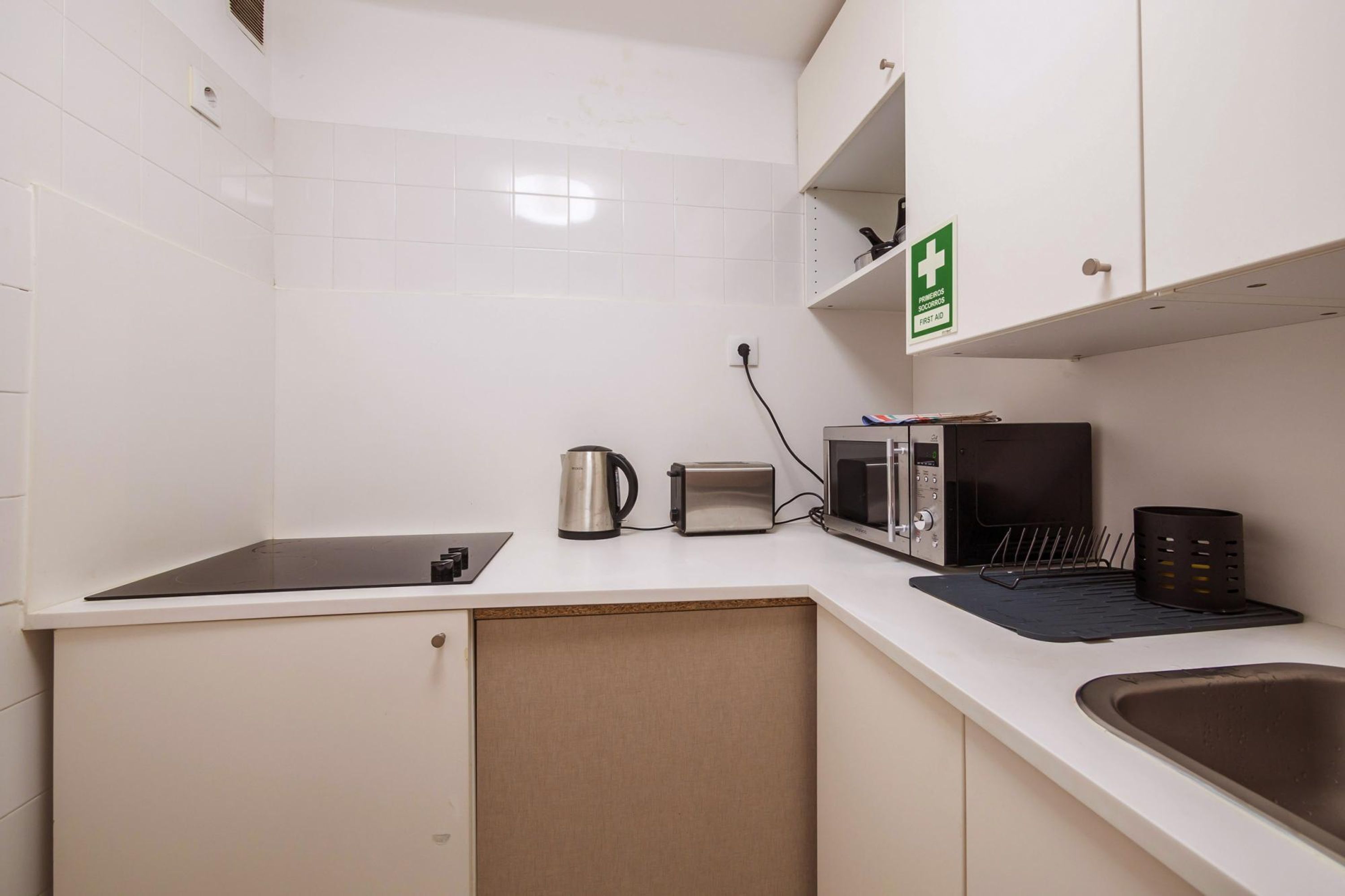 Een kleine kitchenette met een magnetron, broodrooster, waterkoker en een spoelbak.