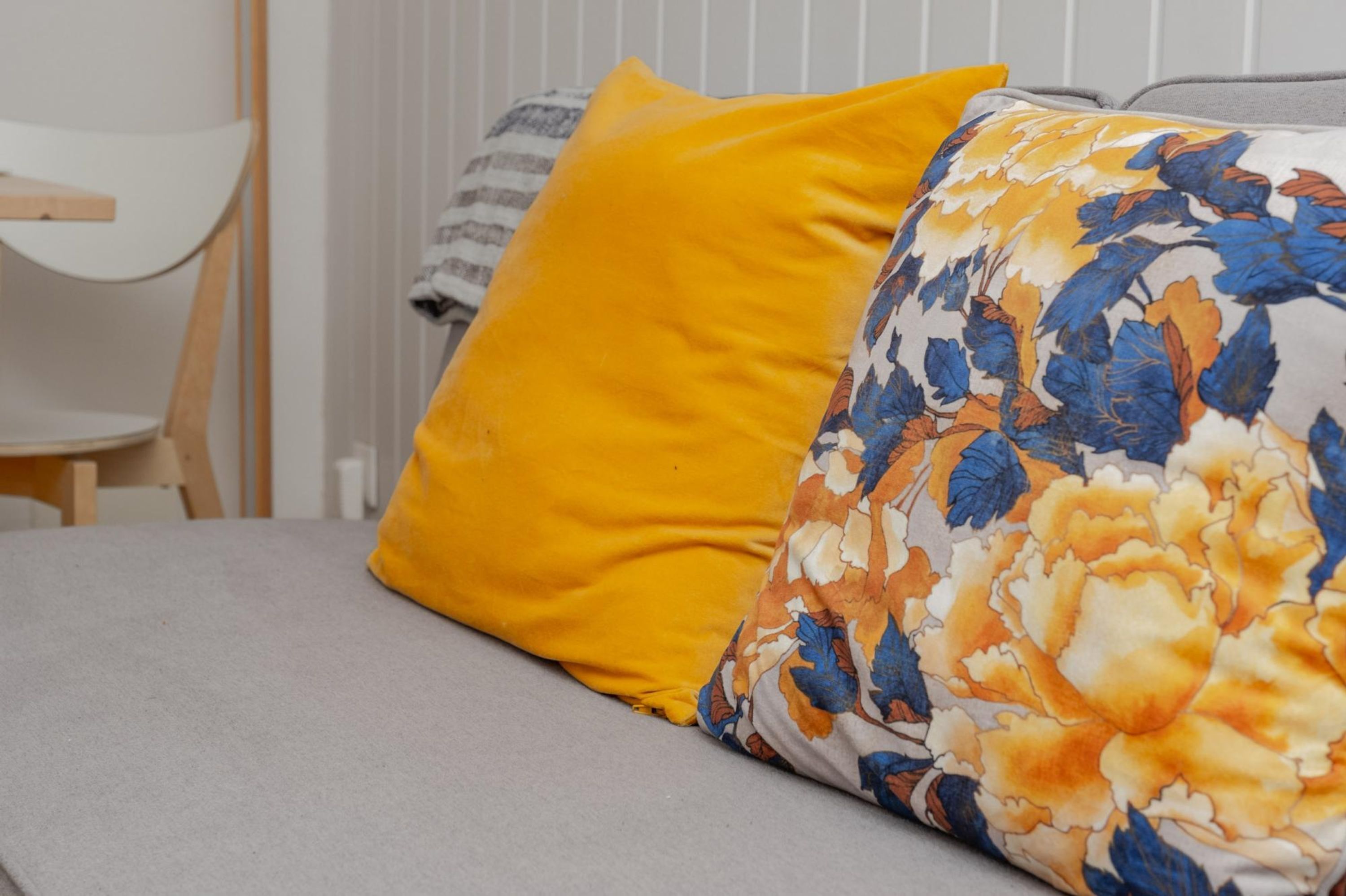 Ein Bett mit grauem Matratze und zwei Kissen, eines gelb und eines mit Blumenmuster.