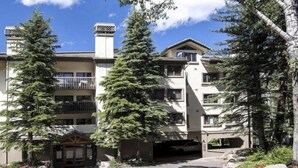 A multi-story building with a balcony, surrounded by tall trees.