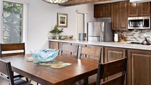 A modern kitchen with wooden cabinets, stainless steel appliances, and a dining area with a wooden table and chairs.