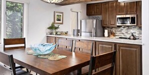 A modern kitchen with wooden cabinets, stainless steel appliances, and a dining area with a wooden table and chairs.