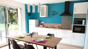 A modern kitchen with a teal accent wall, white cabinetry, and a dining area with a wooden table and black chairs. - Domaine des Hameaux du Lac, 2 Chambres, 6 Pers max (SAINT PARDOUX LE LAC)