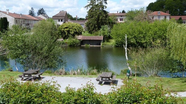 A lakeside view with picnic tables, a wooden bridge, and houses in the background. - Domaine des Hameaux du Lac, 2 Chambres, 6 Pers max (SAINT PARDOUX LE LAC)