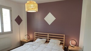 A bedroom with a large bed, two bedside tables with lamps, a window, and a wall with geometric decorations. - Domaine des Hameaux du Lac, 2 Chambres, 6 Pers max (SAINT PARDOUX LE LAC)