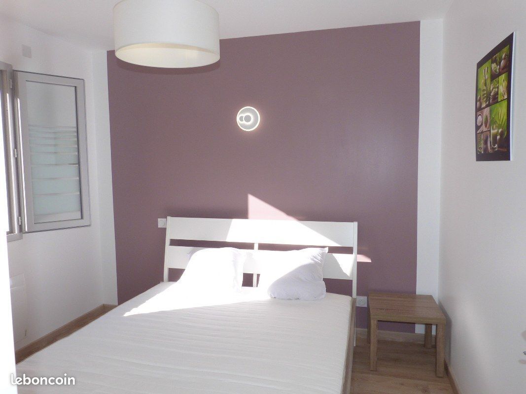 A bedroom with a bed, a bedside table, a window, and a wall-mounted light fixture.