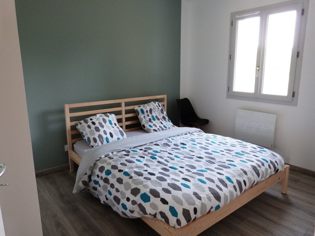Un dormitorio con cama, almohadas, una silla y un ventanal.