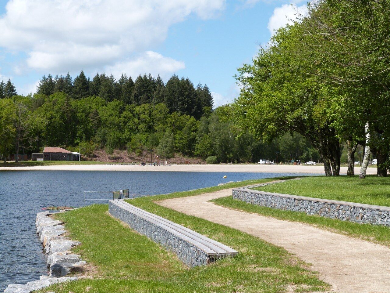 Ein Park am Seeufer mit einem Kiesweg, Rasenflächen und einem Strand in der Ferne.