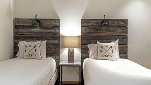 A bedroom with two beds, each with a pillow featuring 'KSI' and arrows. A nightstand with a lamp and a decorative vase is between the beds. - Townsend Place 2 Bedroom Ski-in, Ski-out Condo in Beaver Creek Village (Avon)