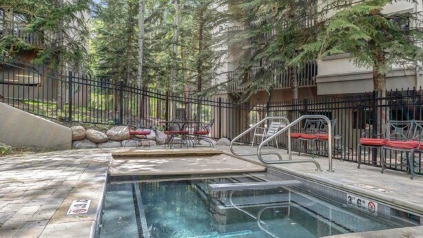 A swimming pool with a diving board, surrounded by a metal fence and trees. - Townsend Place 2 Bedroom Ski-in, Ski-out Condo in Beaver Creek Village (Avon)