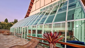 A conservatory with a glass roof, wooden benches, and a potted plant. - Dúplex Luxo com Piscina Aquecida, Lareira e Wifi (Campos do Jordão)