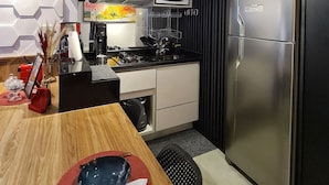 A modern kitchen with a stainless steel refrigerator, a microwave, and a coffee machine. There is a wooden dining table with a bowl and a napkin. - Dúplex Luxo com Piscina Aquecida, Lareira e Wifi (Campos do Jordão)
