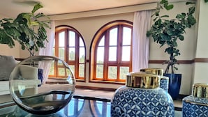 A room with a sofa, a glass table, decorative vases, and large windows with curtains. - Dúplex Luxo com Piscina Aquecida, Lareira e Wifi (Campos do Jordão)